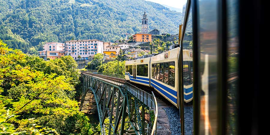 Looking down the side of a blue and yellow train running on the Centrovalli railway.