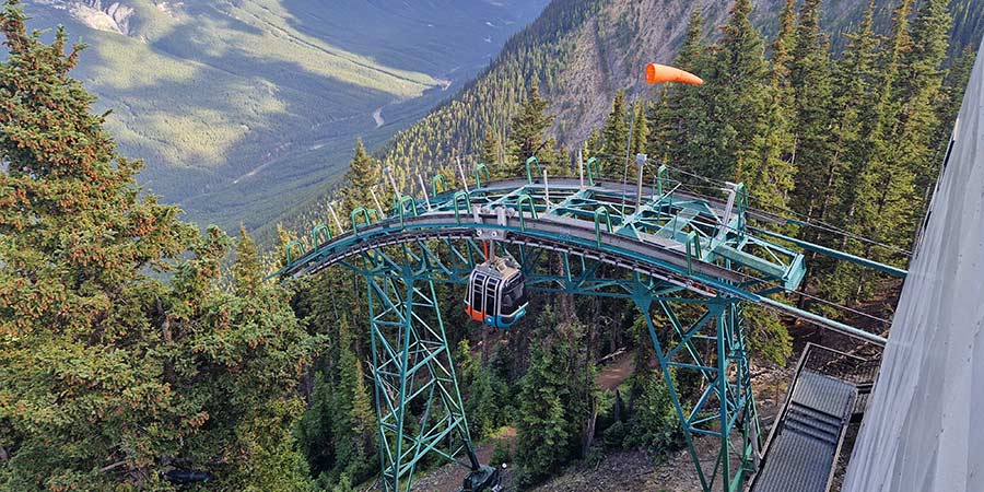 The Banff Gondola hangs above a steep drop, surrounded by the dramatic tree line of Banff National Park.