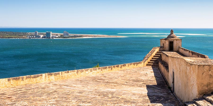 The stone terrace and guardhouse of the Fort of São Filipe in Setúbal overlooks the blue sea on a sunny day.