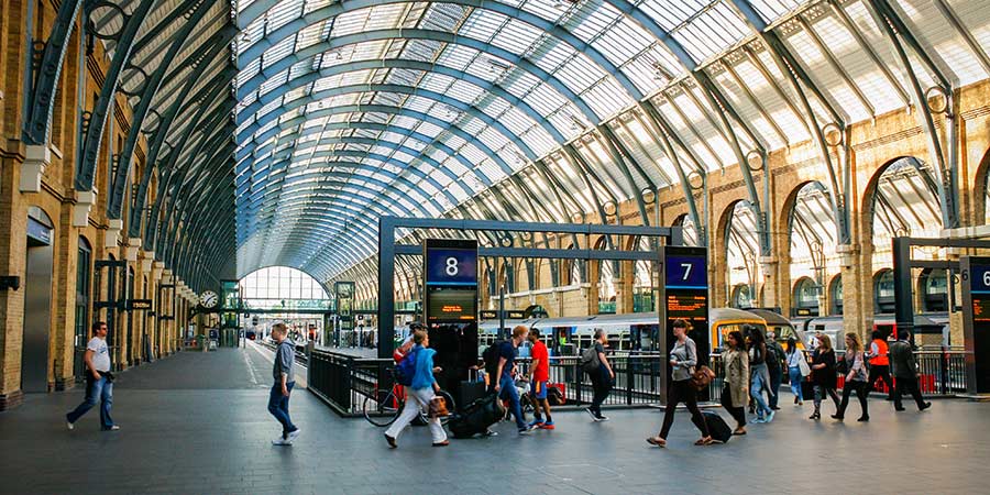 King’s Cross Station in London is full of busy people and trains pulling onto platforms.