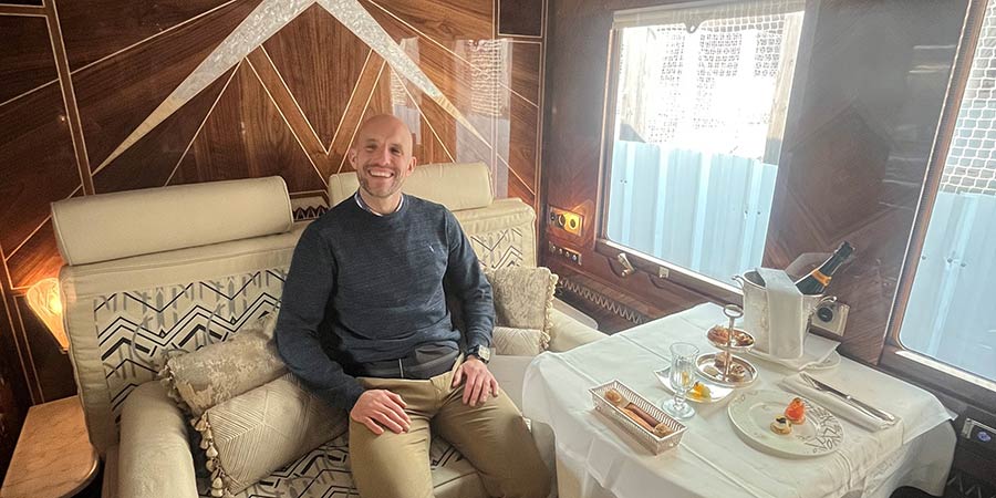 James sits in his luxury suite, with a welcome snack and bottle of champagne on the table.