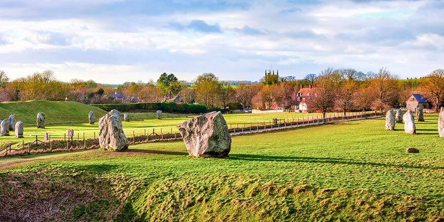 Stone circle, Avebury. A road bisects a stone circle with a number of megaliths. Nearby, is the picturesque village of Avebury