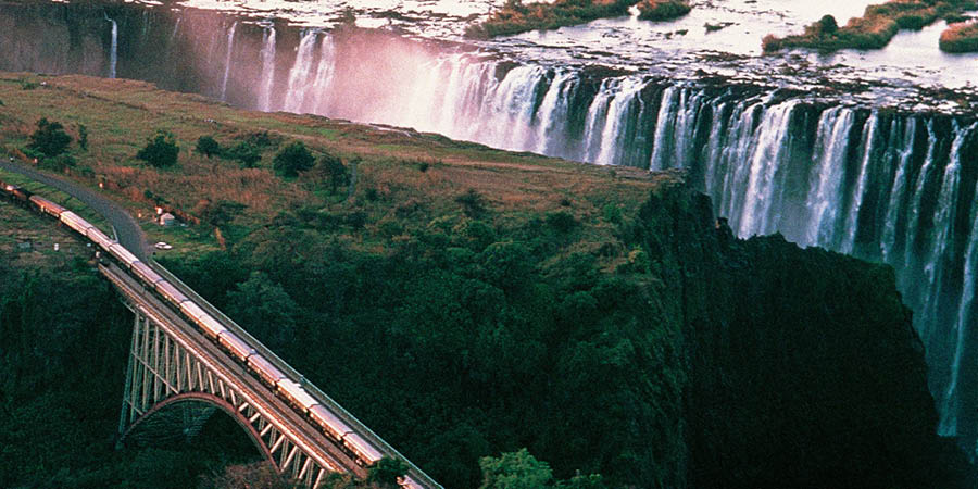 The Rovos Rail train passes over a bridge near a large waterfall. 