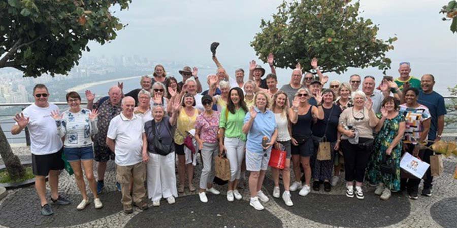 Group of people posing and waving at a scenic viewpoint overlooking Rio de Janeiro, Brazil. 